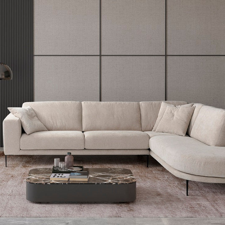 Beige sectional sofa in a modern living room setting with a rug and side table.